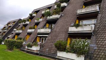 Una hilera de edificios residenciales con techos inclinados, balcones con plantas y una zona verde al frente.