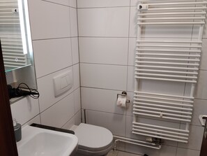 Un baño pequeño con inodoro, lavamanos y toallero, todo en color blanco.