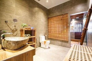 Un baño moderno con un lavamanos de piedra grande, estantes de madera, un inodoro y una ventana con persianas de bambú.