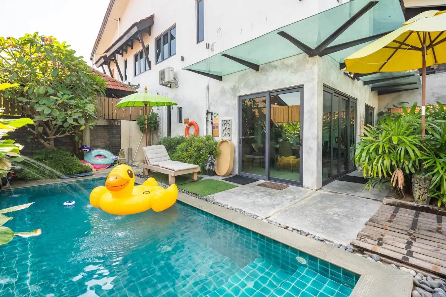 A swimming pool with a rubber duck float, a lounge chair, and a glass-enclosed patio area.