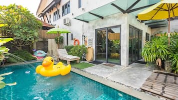 A swimming pool with a rubber duck float, a lounge chair, and a glass-enclosed patio area.