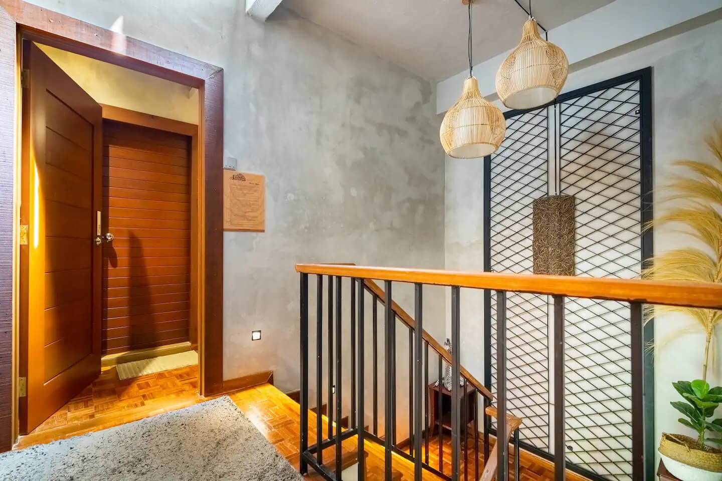 A staircase with a wooden handrail and a metal railing, leading to a room with a wooden door and a textured wall.