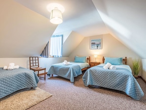 Ein gemütliches Schlafzimmer im Dachgeschoss mit drei Betten, einem Holzstuhl, einem kleinen Tisch und einem Fenster mit Vorhängen.