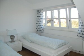 A single-bed room with a window, a bedside table with a lamp, and curtains with a polka dot pattern. - Holiday apartment with 2 bedrooms (Langeoog)
