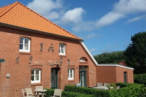 A brick building with a red-tiled roof, multiple windows, and a small outdoor seating area with chairs and tables. - Holiday apartment with 2 bedrooms (Langeoog)