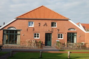 Een gebouw van baksteen met een pannendak, een groene deur en een raam met een witte omlijsting.