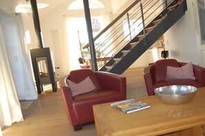 A modern living room with a fireplace, red sofas, a wooden coffee table, and a staircase. - Holiday apartment with 2 bedrooms (Langeoog)