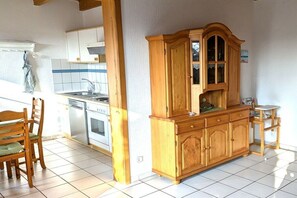 A kitchen with white cabinets, a wooden cabinet, a dining table with chairs, and a small stool. - Holiday home with 3 bedrooms (Wangerland-Hooksiel)