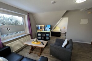 A living room with a television, a sofa, a coffee table, and a window with blinds. - Holiday apartment in Sylt with 2 bedrooms (Westerland)