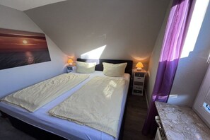A hotel room with a bed, two bedside tables, a nightstand, a window with curtains, and a painting on the wall. - Holiday apartment in Sylt with 2 bedrooms (Westerland)