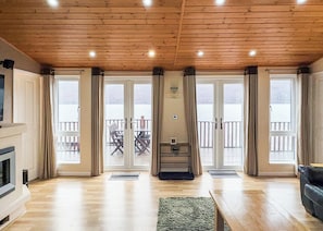 A spacious living room with a wooden ceiling, large sliding glass doors leading to a balcony, and a fireplace. - 2 bedroom accommodation in Invermoriston (Invermoriston)