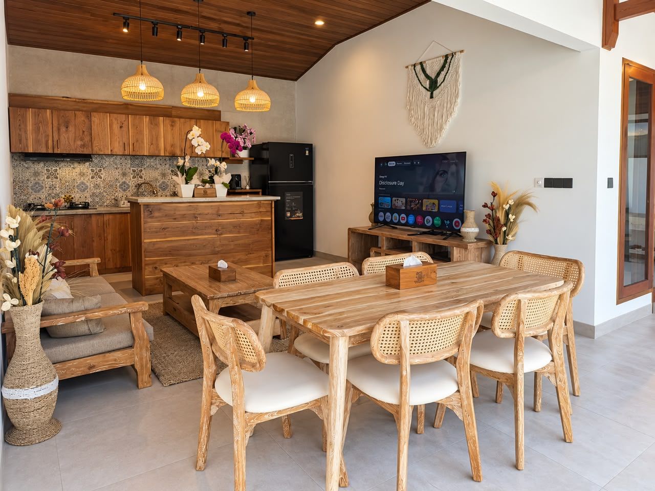 Une cuisine moderne avec des meubles en bois, un réfrigérateur noir et un coin repas comprenant une table en bois et des chaises en osier.