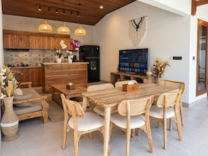 Cozinha moderna com armários de madeira, geladeira preta e área de refeições com mesa de madeira e cadeiras de vime.