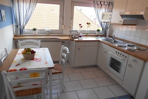 Une cuisine compacte comprenant une table à manger, des chaises, un four à micro-ondes, un four traditionnel et une fenêtre avec des rideaux.