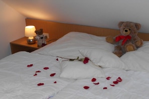 A bed with white bedding, a teddy bear, and rose petals scattered on it. - My North Sea happiness (Horumersiel)