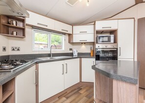 A modern kitchen with a gas stove, a microwave, and an oven. There is a window above the sink, and wooden cabinets. - Modern two-bedroom holiday home. (Fort Augustus)