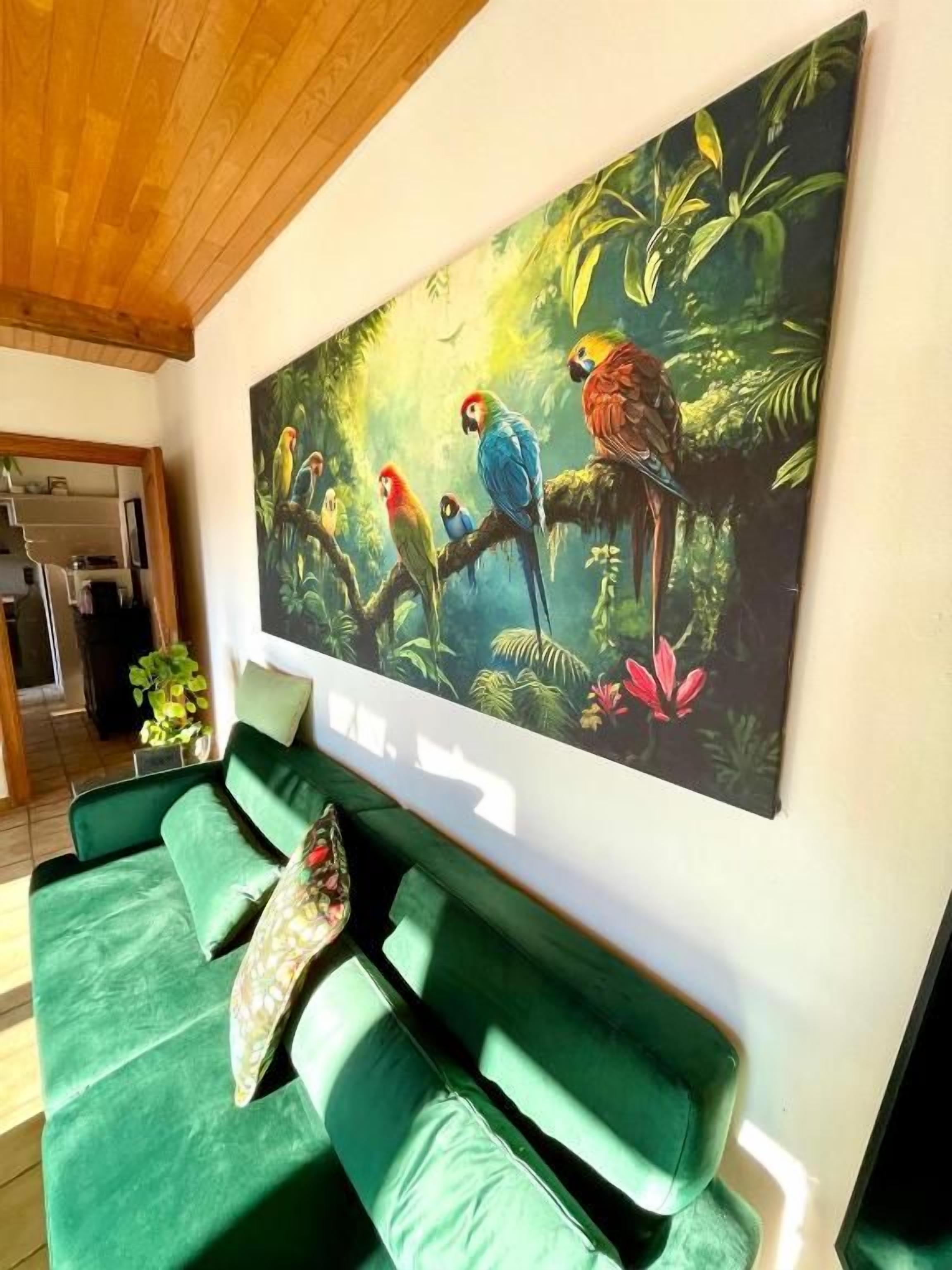 A room with a green sofa, a large painting of colorful birds, and a wooden ceiling.