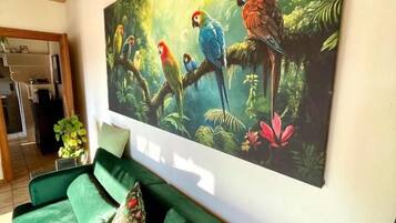 A room with a green sofa, a large painting of colorful birds, and a wooden ceiling.