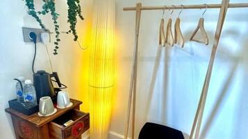 A room with a wooden floor, a hanging plant, a lamp, a wooden table with items, and a swing with a basket seat.