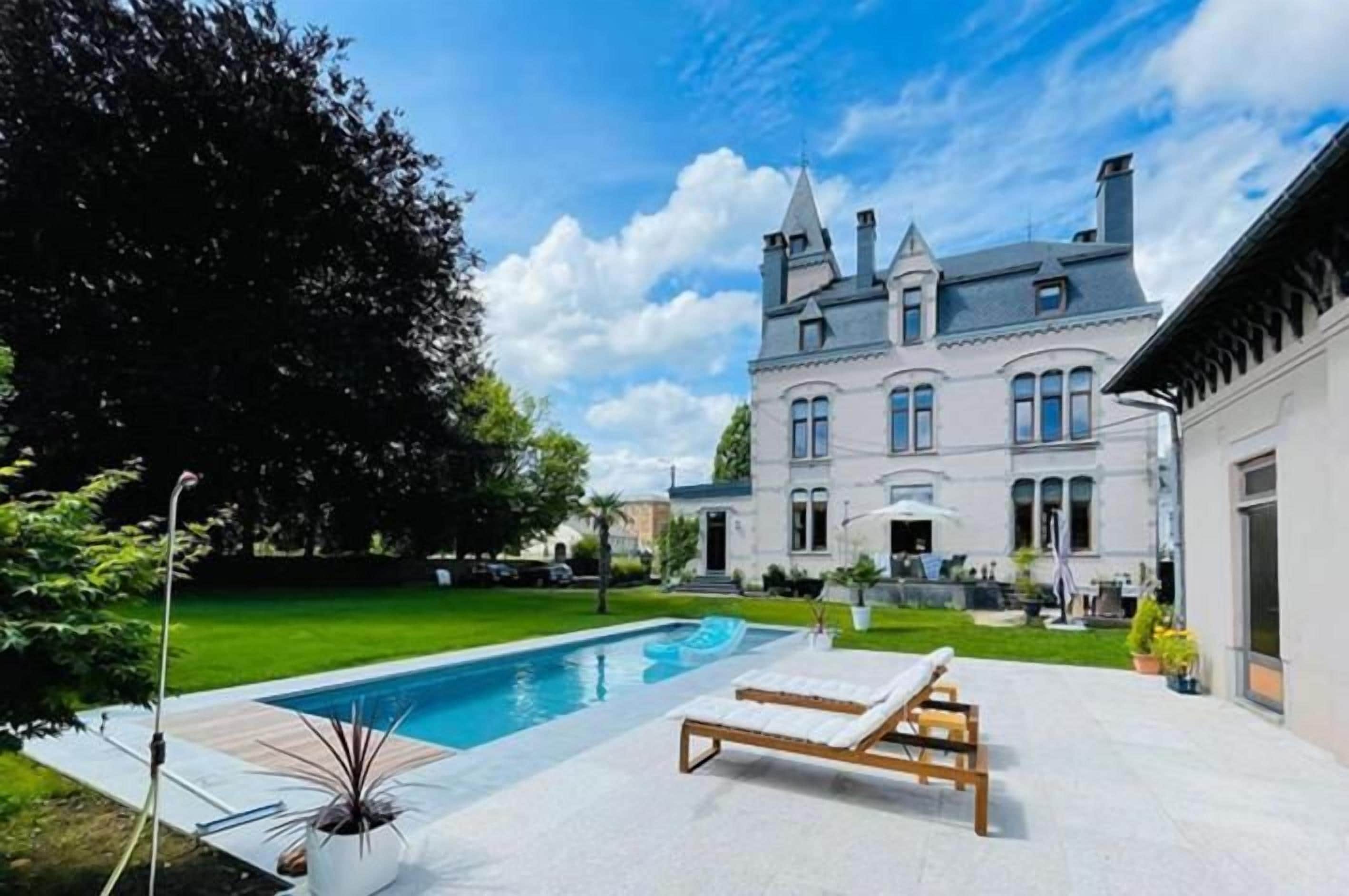 Ein großes Haus mit Schwimmbad und Liegestuhl.