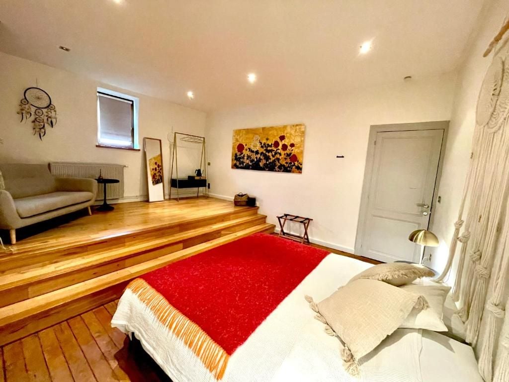 Quarto com cama, tapete vermelho, sofá, janela e porta.