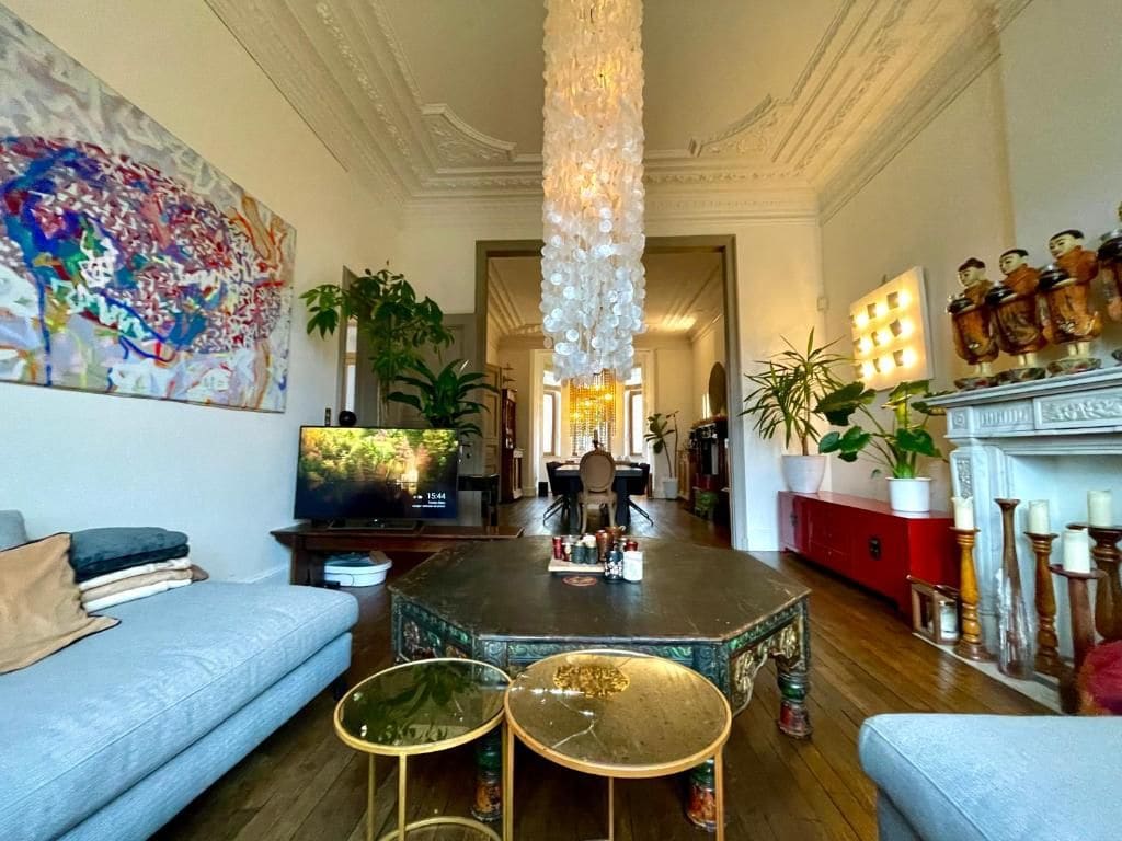 Una sala de estar con candelabro, televisor, chimenea y un cuadro abstracto grande.