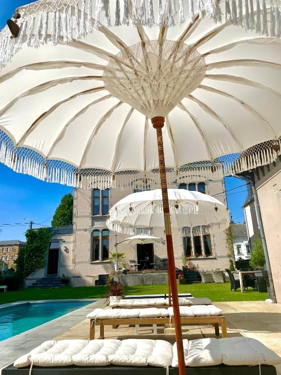 Un área junto a la piscina con una gran sombrilla blanca, sillas de descanso y un edificio al fondo.