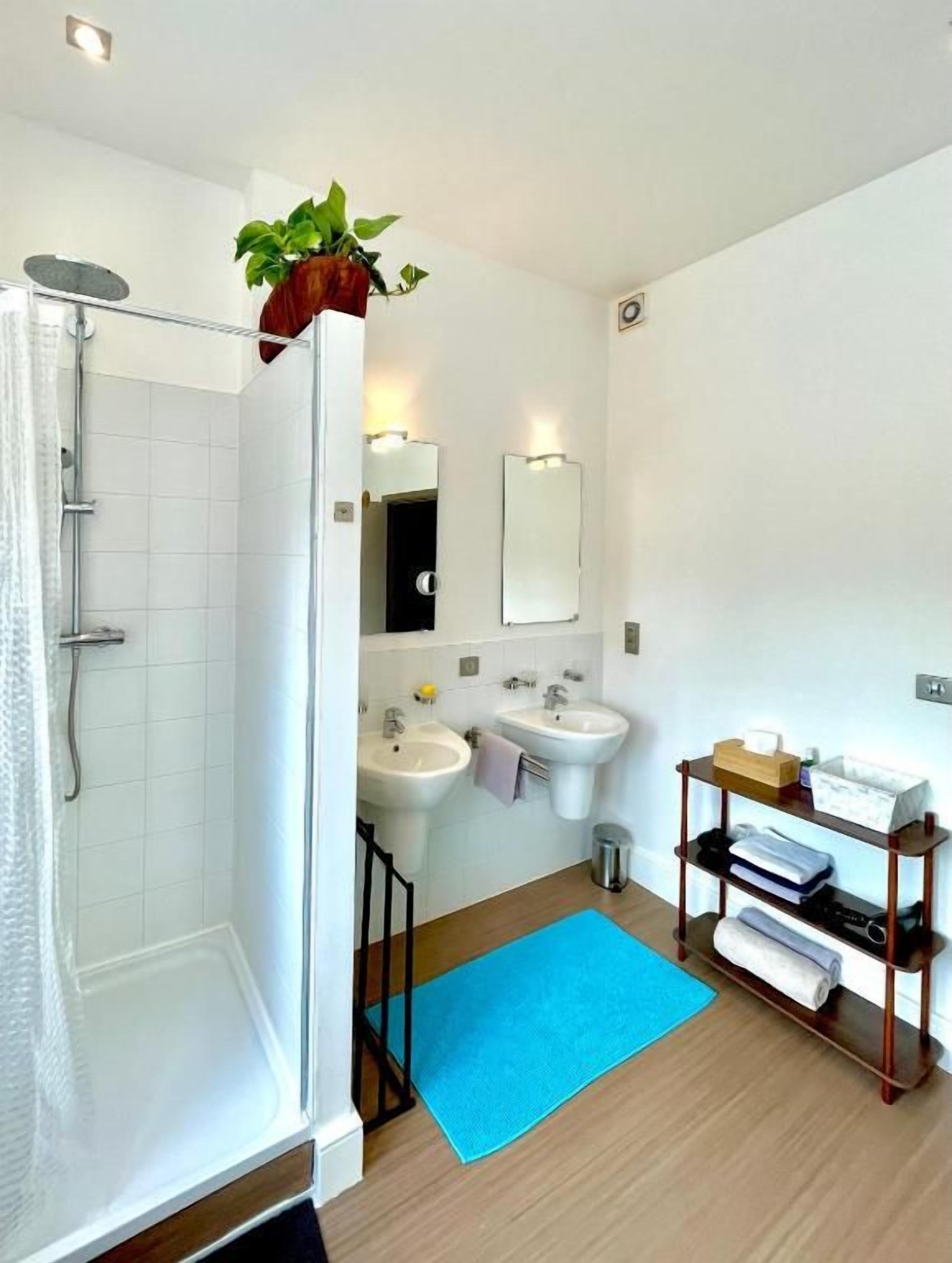 Een moderne badkamer met een douche, twee wastafels, een spiegel en een plank met handdoeken.