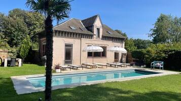 Een huis met een zwembad, terras en een palmboom.