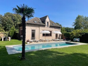 A house with a swimming pool, outdoor seating, and a palm tree.