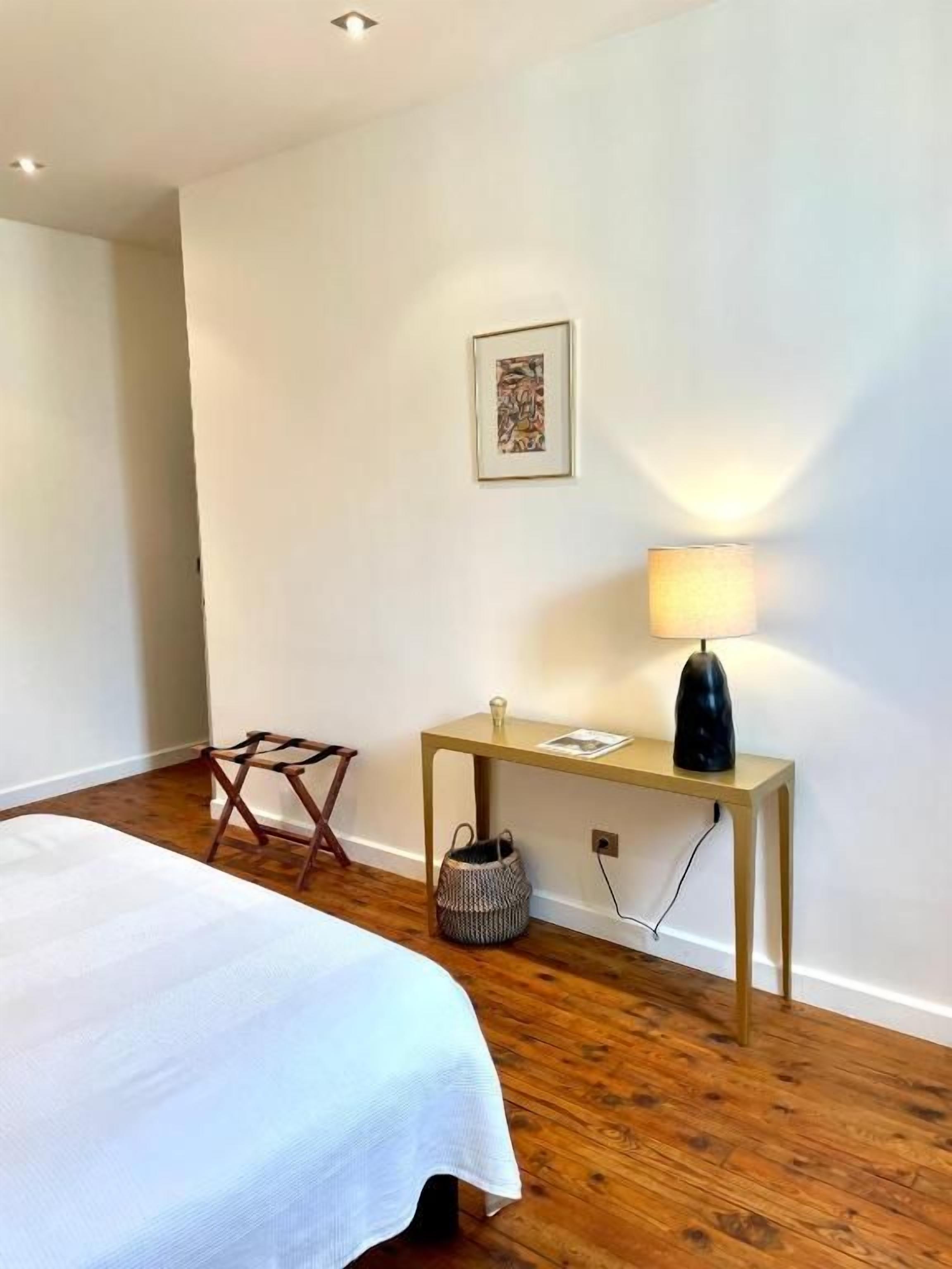 A hotel room with a bed, a desk, a lamp, a wall-mounted picture, and a wooden floor.