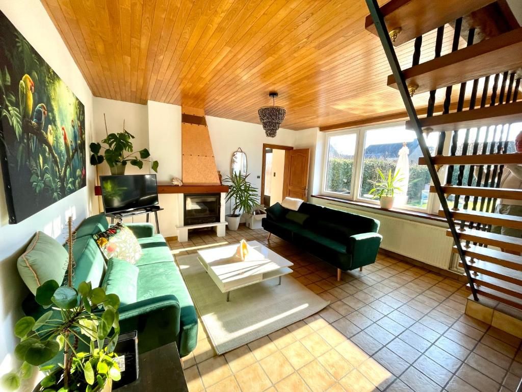A spacious living room with a green sofa, a white coffee table, and a fireplace. There is a large window providing a view of the outdoors.