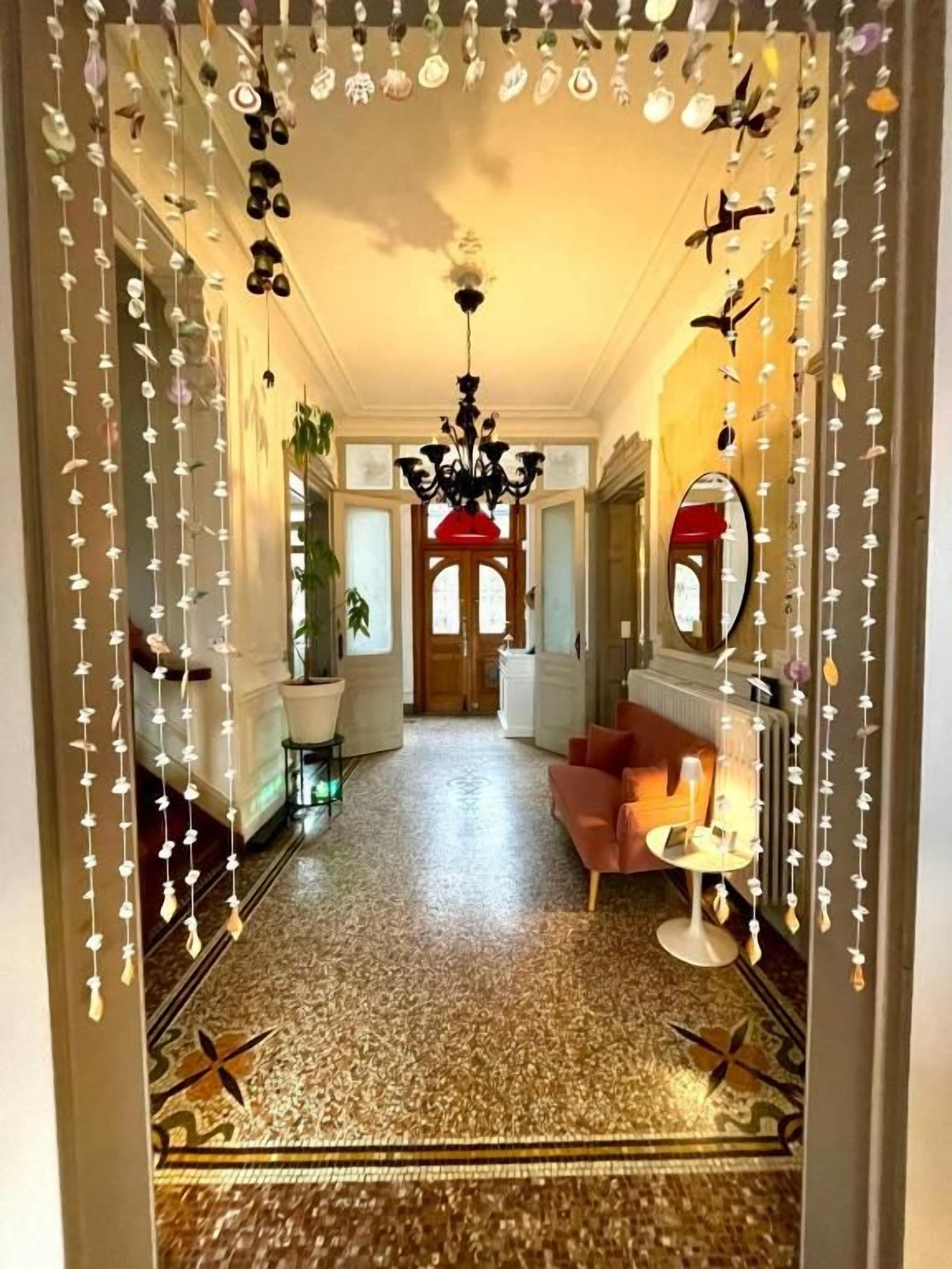 Un couloir doté d’un sol à motifs, d’un lustre et d’un miroir à cadre rouge.