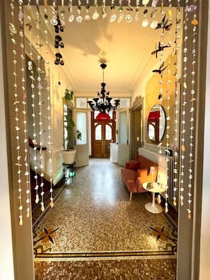 A hallway with a patterned floor, a chandelier, and a red-framed mirror.