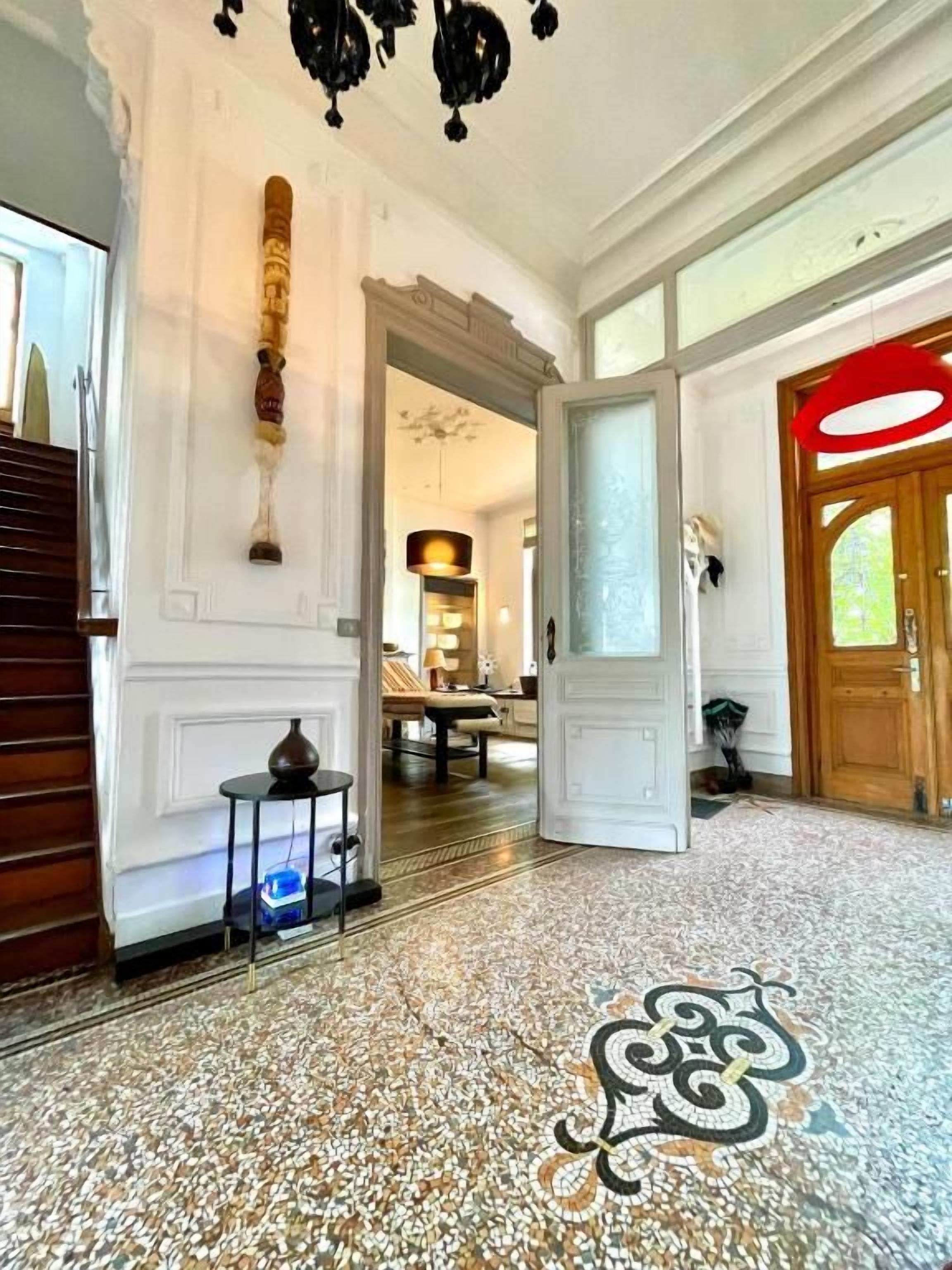 Un hall d’entrée spacieux, doté d’un sol à motifs, d’un escalier en bois et d’une grande porte en bois.