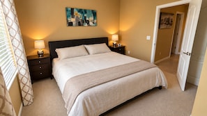 A bedroom with a large bed, two bedside tables with lamps, a painting on the wall, and a door to another room. - Furnished Pool Home with Beautiful Lake Views in Stoneybrook at Venice (Venice)