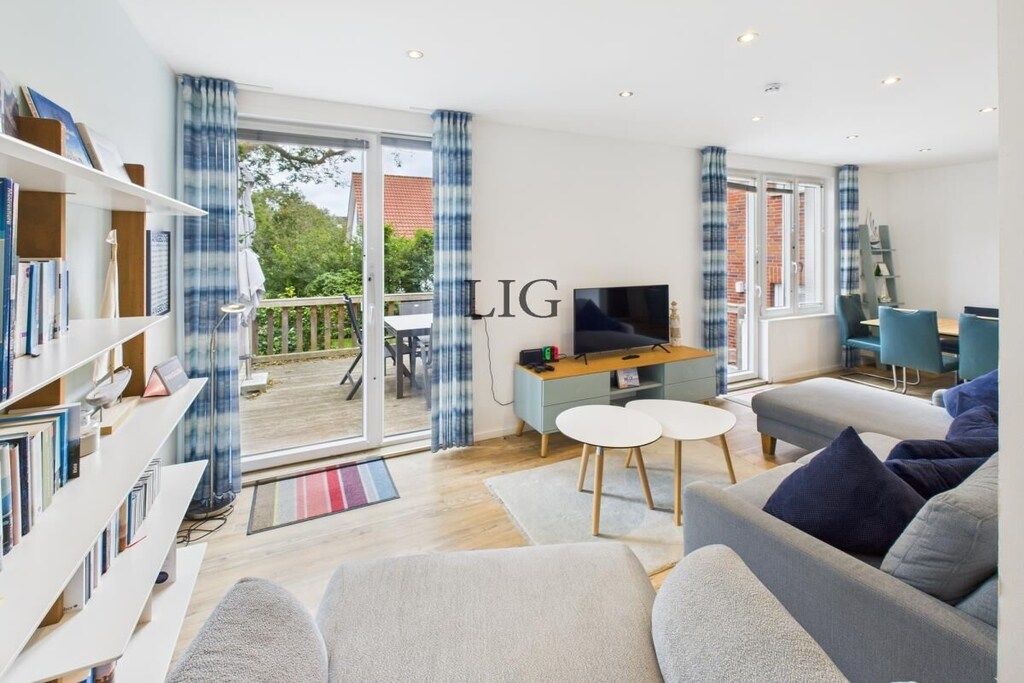 A modern living room with a sofa, TV, bookshelf, and a balcony with a table and chairs.