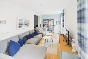 A modern living room with a sofa set, a coffee table, a bookshelf, and a television. - Holiday apartment with 1 bedroom (Langeoog)