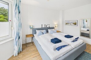 A bedroom with a bed, a nightstand, a wall-mounted lamp, a window with curtains, and a framed picture. - Holiday apartment with 1 bedroom (Langeoog)