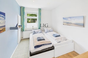 Een slaapkamer met twee bedden, een raam met gordijnen, een radiator en een aan de muur hangend kunstwerk.