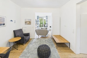 Een moderne woonkamer met een grijze bank, een rond poefje, een klein houten tafeltje en een bankje.