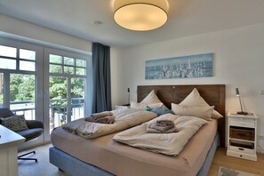 Camera da letto moderna con un letto grande, una scrivania e vista su spazi verdi.