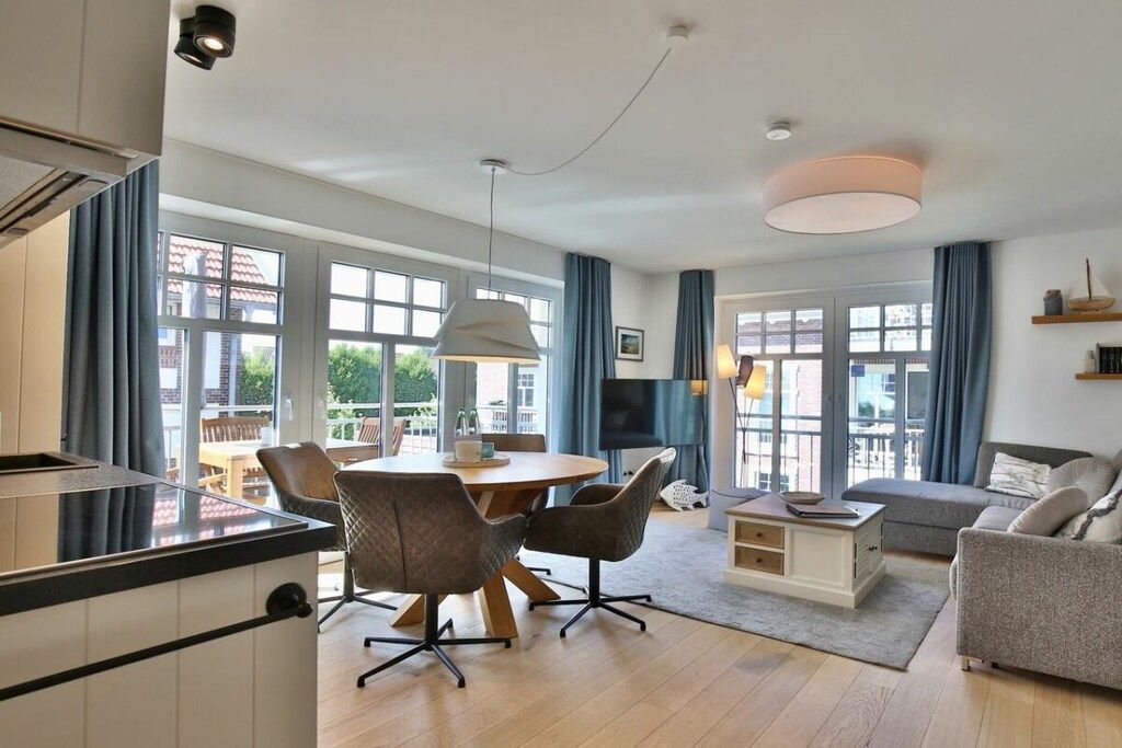A modern living room with a dining area, large windows, and a flat-screen TV.