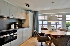 A modern kitchen with grey cabinets, a built-in oven, and a dining area with a round table and chairs. - Holiday apartment Inselherz (Wangerooge)
