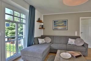 A modern living room with a grey sectional sofa, a coffee table, and a painting on the wall. - Holiday apartment Inselherz (Wangerooge)