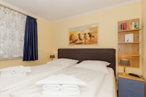 A hotel room with a bed, a painting, a bookshelf, and a window with curtains. - Holiday apartment Haus Atlantik 319553 (Kühlungsborn - Ost)