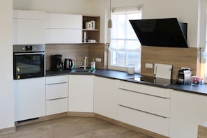 A modern kitchen with white cabinets, a built-in oven, a coffee maker, and a window with a view. - Thatched house "Blinkfor" (Zierow)