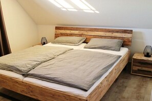 A bedroom with a wooden headboard, two beds with grey bedding, bedside tables with lamps, and a sloped ceiling with skylight. - Thatched house "Blinkfor" (Zierow)