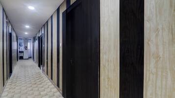 A hallway with alternating dark and light wooden doors, a patterned floor, and recessed ceiling lighting.