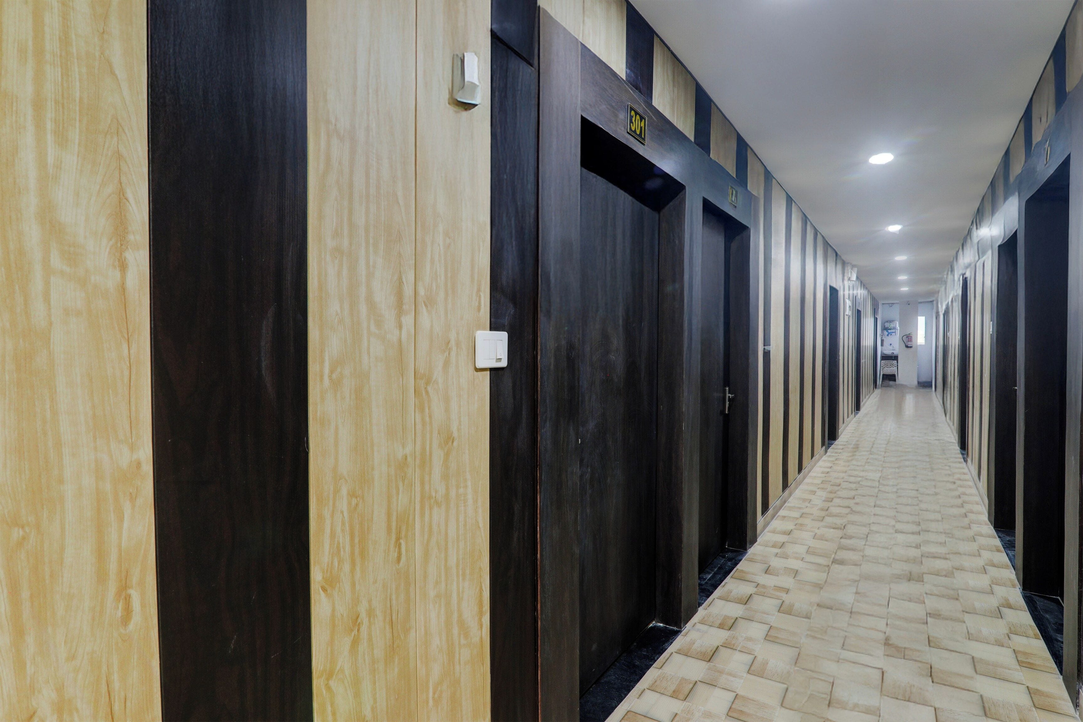 A hotel corridor with alternating dark and light wooden doors, a tiled floor, and a sign indicating room number 301.